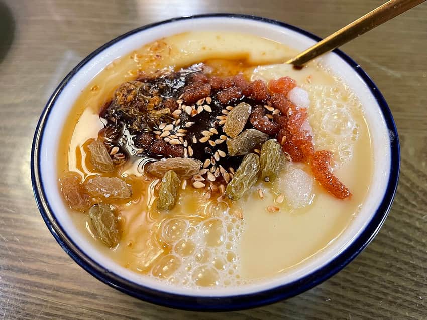 Close bowl of Beijing cha tang with syrup, raisins, sesame and preserved-fruit toppings