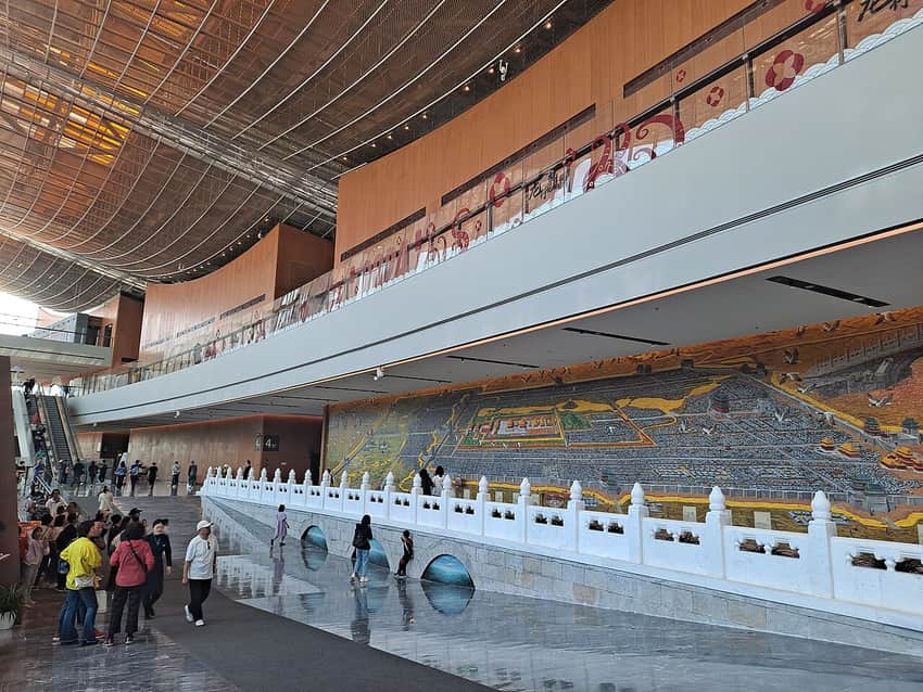Visitors inside the Beijing Grand Canal Museum with a bridge installation and mural