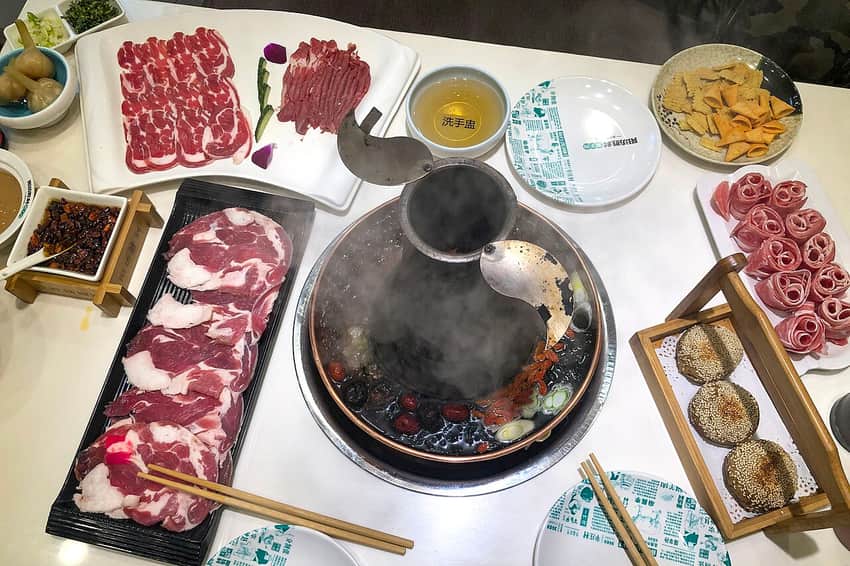 Overhead spread of copper-pot mutton hotpot, raw lamb and accompaniments