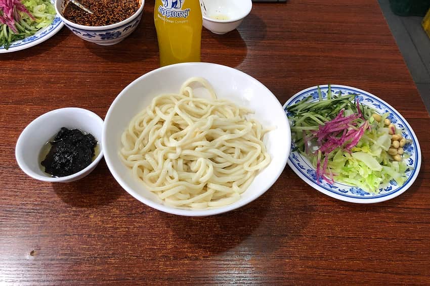 Bowl of noodles, dark sauce and assorted vegetable toppings for zhajiangmian