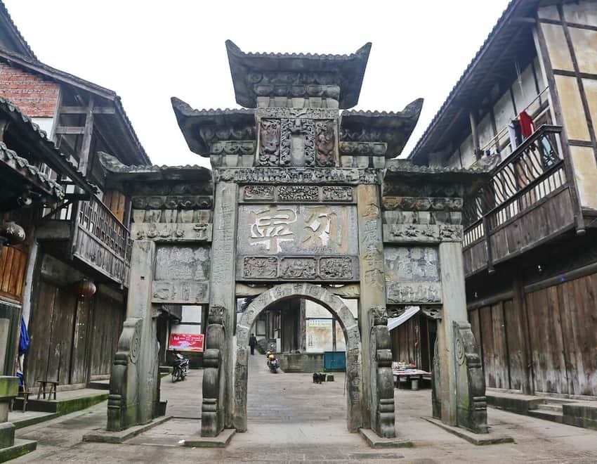 Carved stone archway within the living timber streetscape of Shiqiao