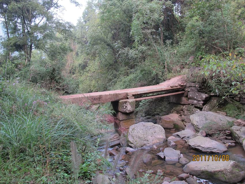 Narrow stone-slab footbridge over a forest stream near Miaoya