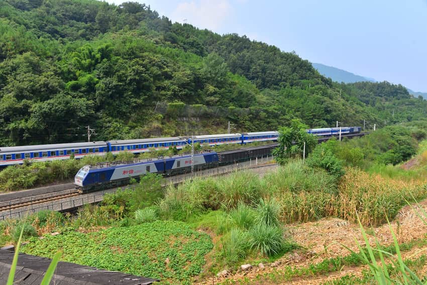 Freight and passenger trains passing through cultivated mountain terrain in Xuanhan