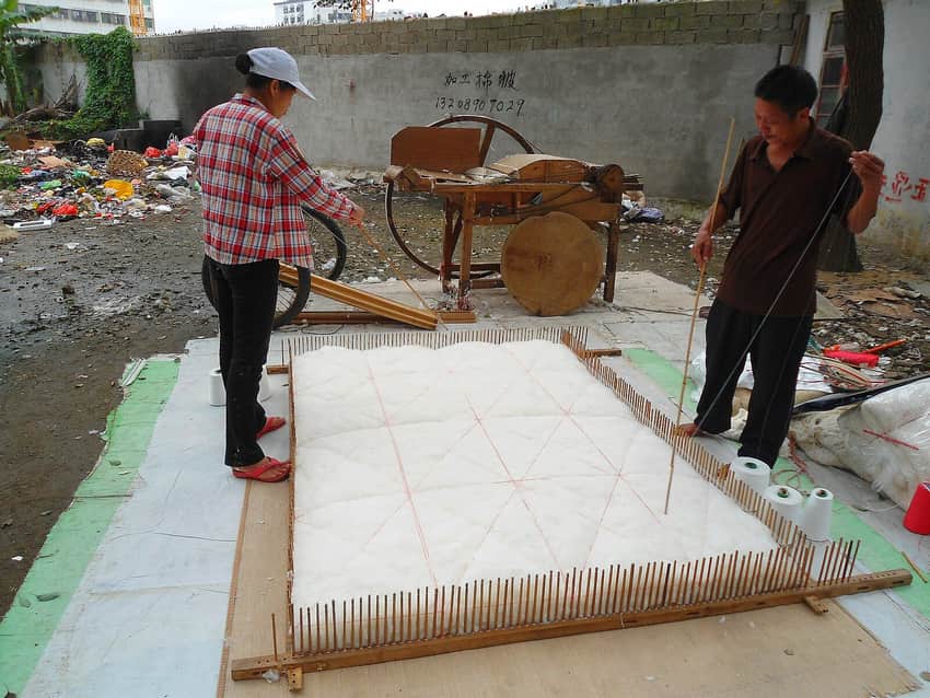Workers stretching thread across cotton batting in a Haikou workshop