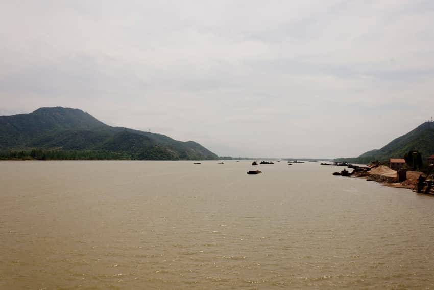 Broad Fuchun River with green hills, barges and developed banks