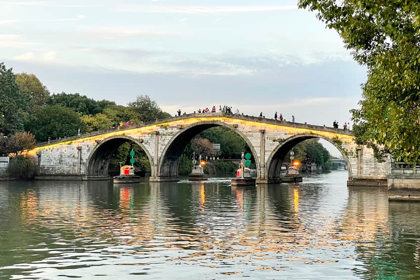 Three-arch Gongchen Bridge with pedestrians and working boats at dusk