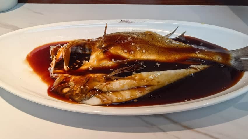 Whole fish covered in dark glossy vinegar gravy on an oval plate