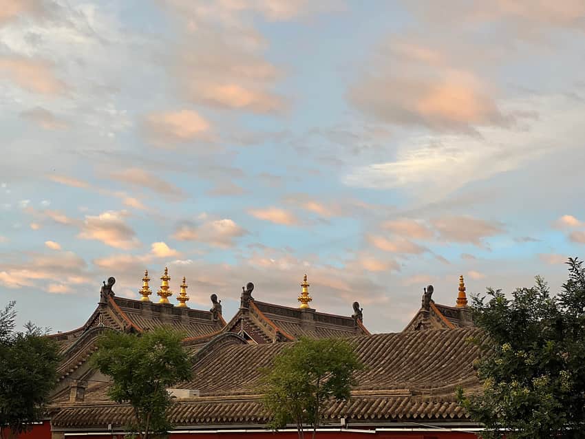 Grey tiled roofs and gilded finials at Dazhao beneath warm evening cloud