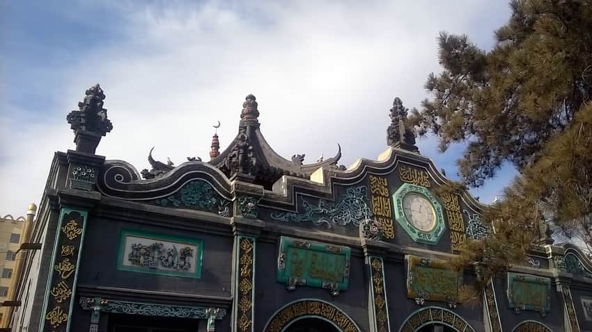 Dark prayer-hall facade with crescent, clock and Arabic calligraphy