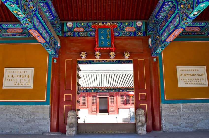 Painted threshold, plaque, stone lions and red courtyard buildings at the Princess Mansion