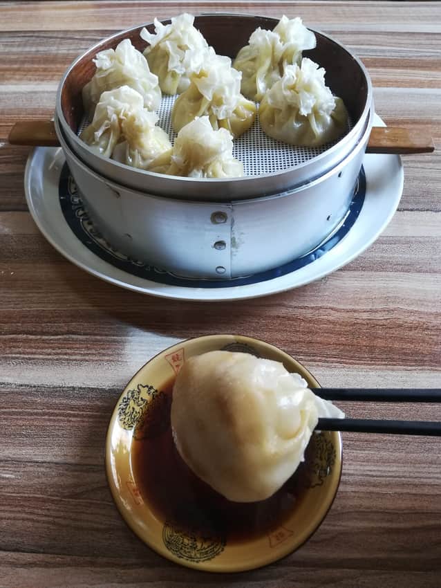 Steamer of lamb shaomai with one dumpling held above a vinegar bowl