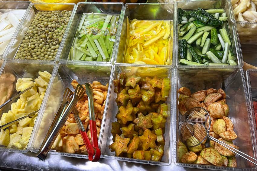 Metal trays of pickled fruit and vegetables at a Nanning suanye stall