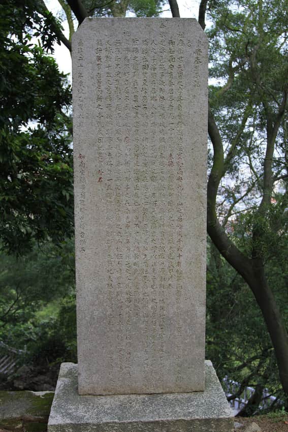 Tall freestanding inscribed stele in the wooded Jiuri Mountain landscape