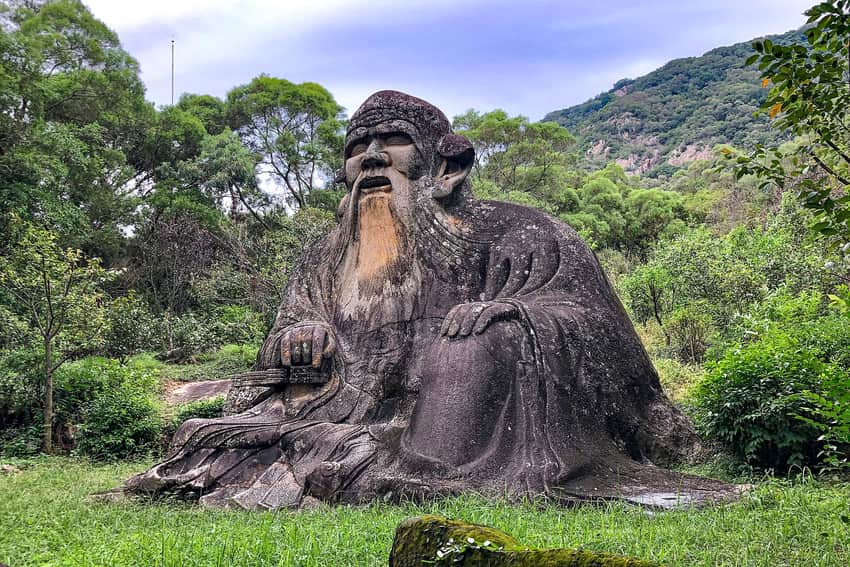 Large seated rock-cut Laozi statue against woodland on Qingyuan Mountain