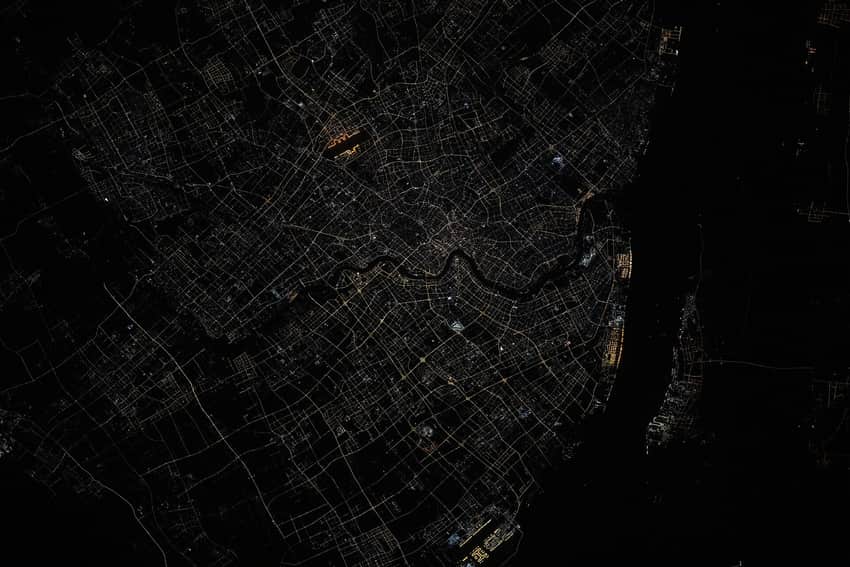Orbital night view of Shanghai's illuminated street grid and dark Huangpu River