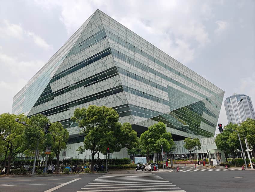 Faceted glass exterior of Shanghai Library East above a tree-lined street