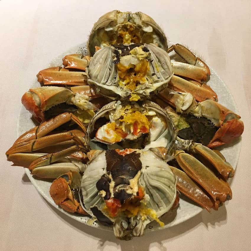 Several cooked mitten crabs opened to show shells, legs and roe on a plate
