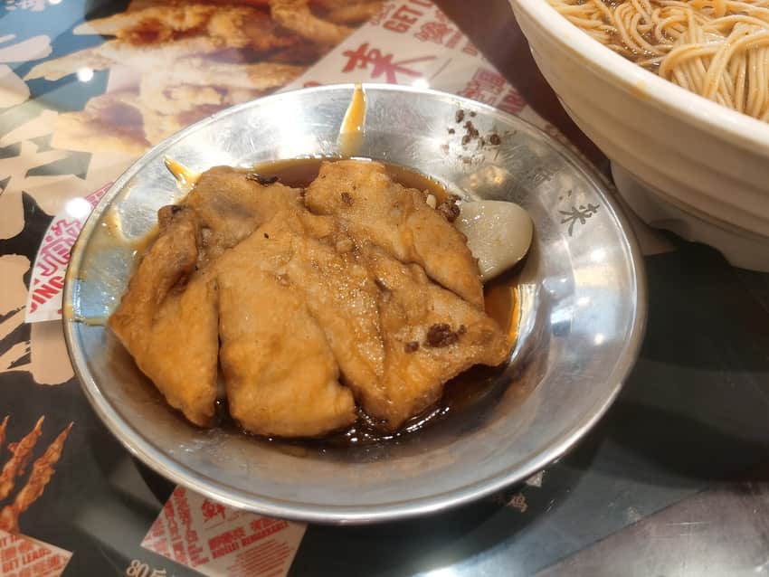 Fried pork pieces and pale rice-cake slices in brown sauce on a metal plate