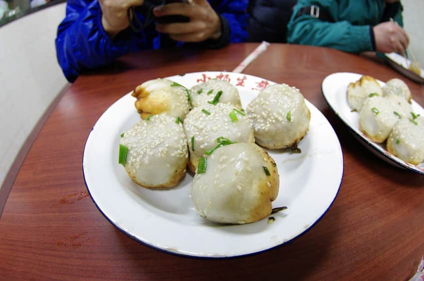 Sesame-and-scallion-topped shengjian buns with browned bases on enamel plates
