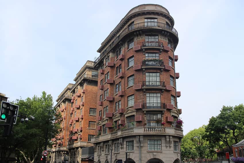 Red-brick Wukang Mansion curving to a narrow point at a tree-lined intersection