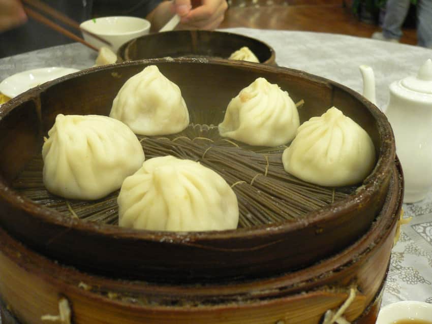Six pleated xiaolongbao in a bamboo steamer on a restaurant table