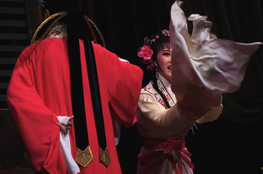 Two Yue-opera performers in embroidered costumes with long sleeves on a dark stage