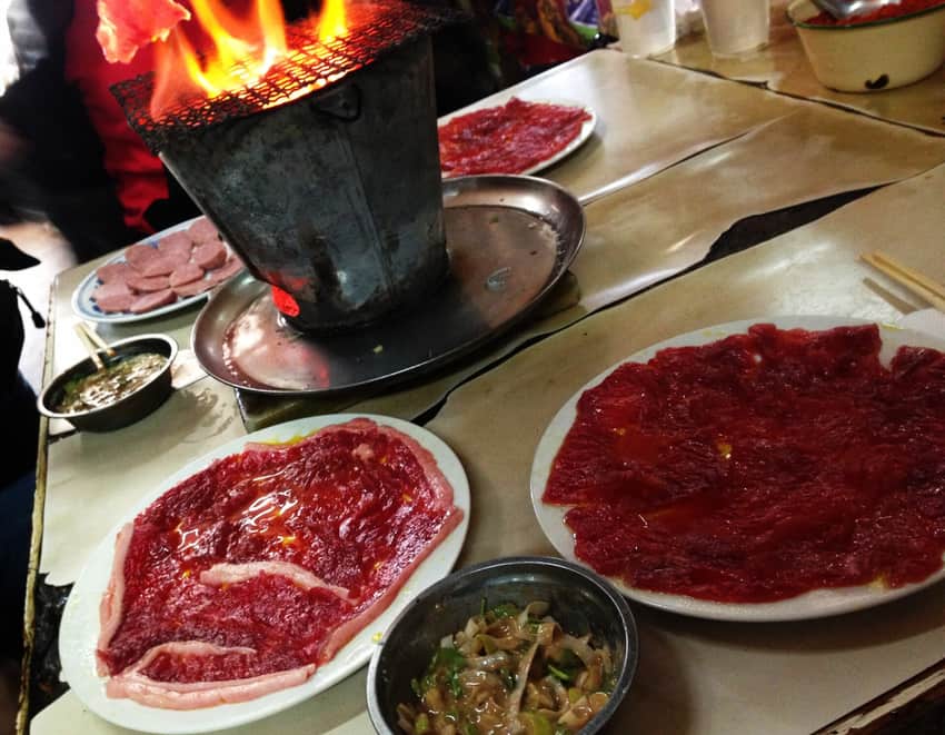 Thin raw meat around a tall charcoal brazier and mesh grill