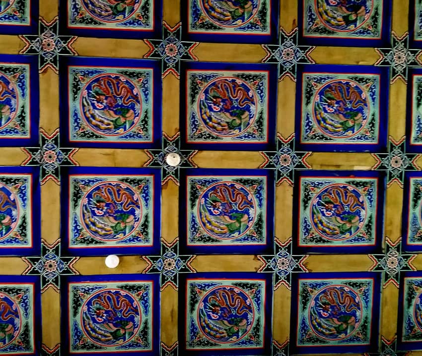 Repeated painted dragon medallions and modern lights on a palace ceiling