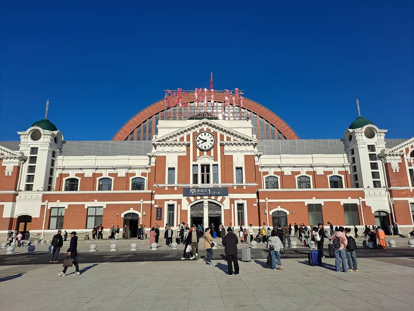 Red-and-white Shenyang Railway Station facade and passengers in 2024