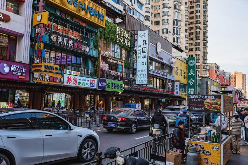 Chinese and Korean shop signs, traffic and a food stall on Xita Street in 2026
