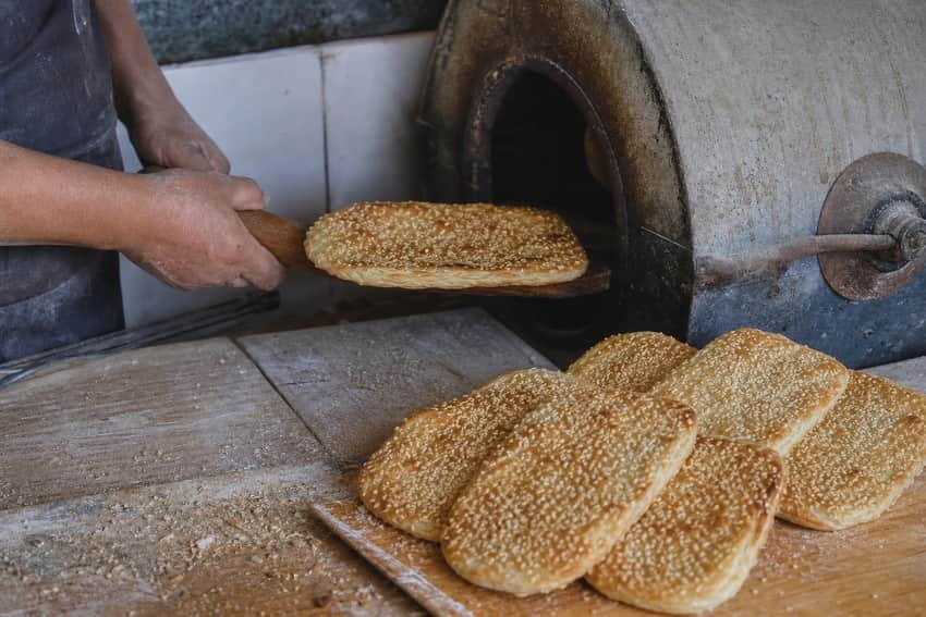 Editorial reconstruction of small sesame ganglu shaobing beside an oven and working hands