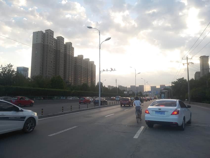 Backlit cyclist, traffic, trees and high-rises on a dated Shijiazhuang street