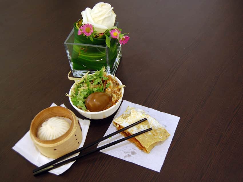 Composed restaurant table with steamed bun, rolled crepe and egg-topped bowl