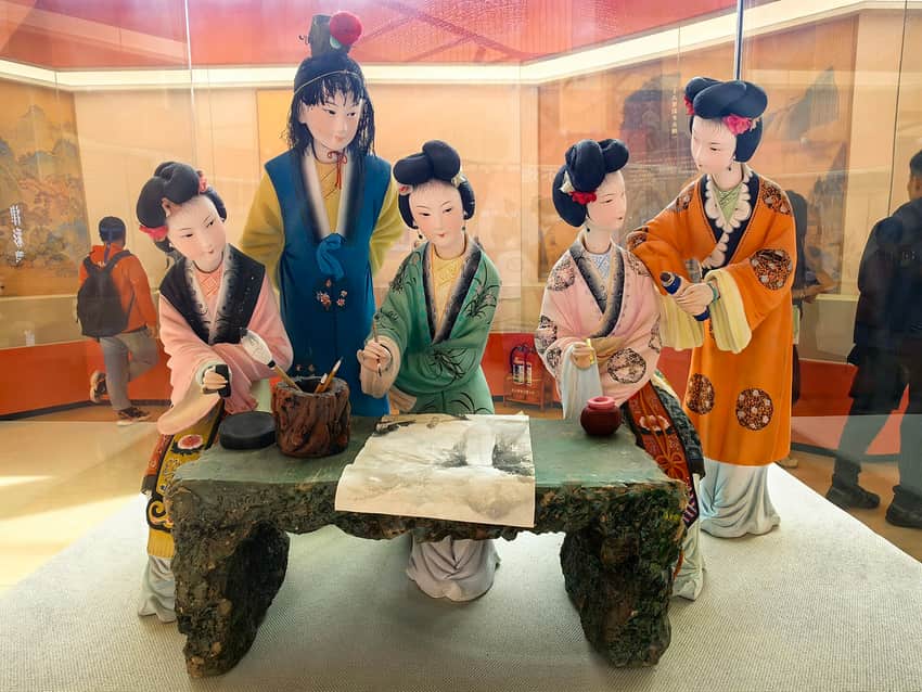 Painted-clay female figures around a painting table in a museum display