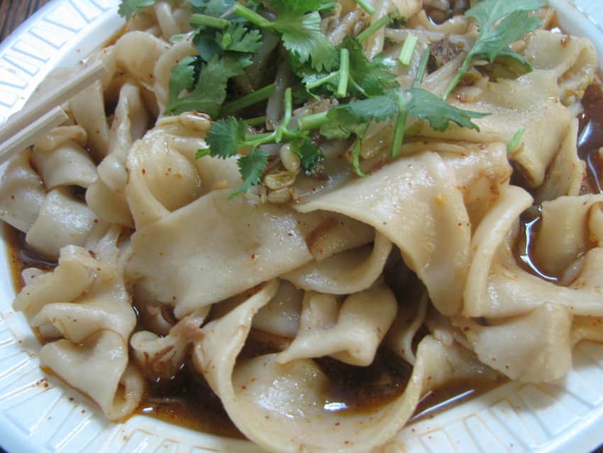 Close bowl of broad biangbiang noodles with coriander and chili seasoning