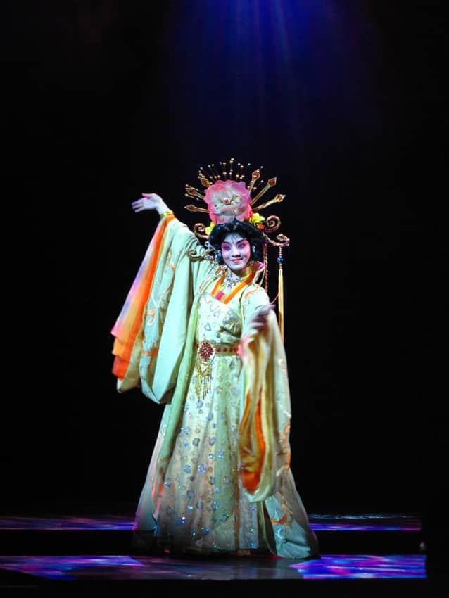 Costumed Qinqiang performer in a stylized pose under blue stage light
