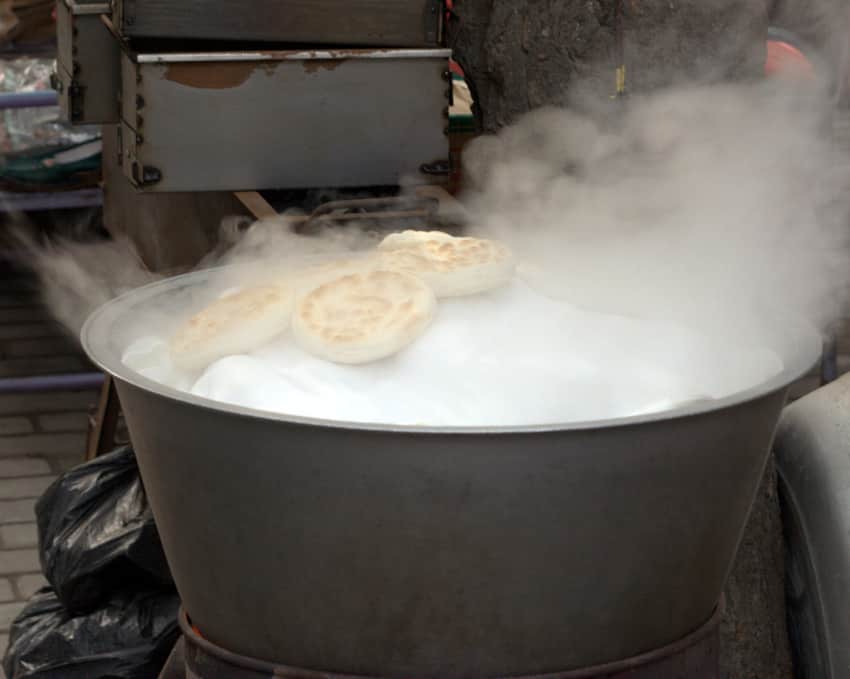 Round flatbreads surrounded by steam above a large metal vessel