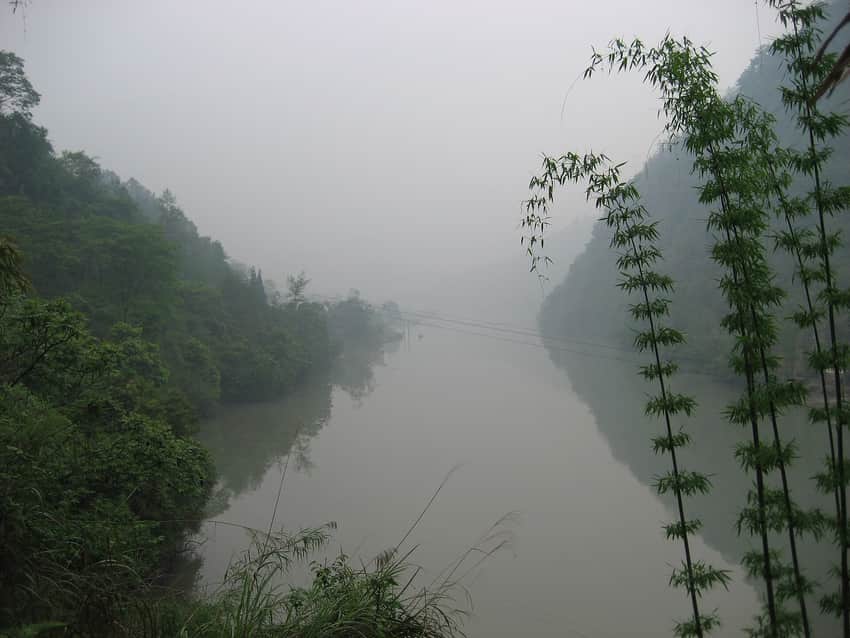 Misty wooded valley reflected in still water at Yingjing